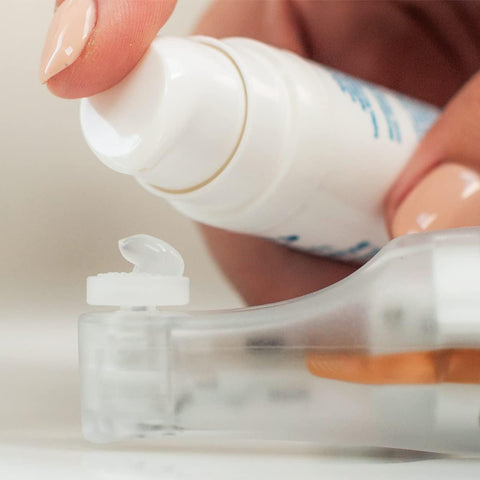 A person applies NuSight Medicals NuLids All Natural At-home Dry Eye Treatment gel from a white pump bottle onto a contact lens case lid, showcasing detailed self-care with nude-manicured nails as part of their essential dry eye relief routine.