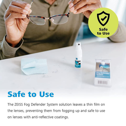 A person holds eyeglasses, a microfiber cloth, and a Zeiss spray bottle on a table. A Safe to Use badge is visible. The ZEISS Fog Defender System promises fog-free vision and protects lenses with anti-reflective coatings.