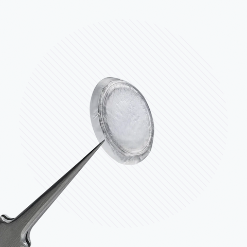 A clear, circular Prokera Amniotic Membrane from BioTissue sits on a metal tool against a white, striped background, highlighting its transparency and precise placement for regenerative healing and corneal protection.